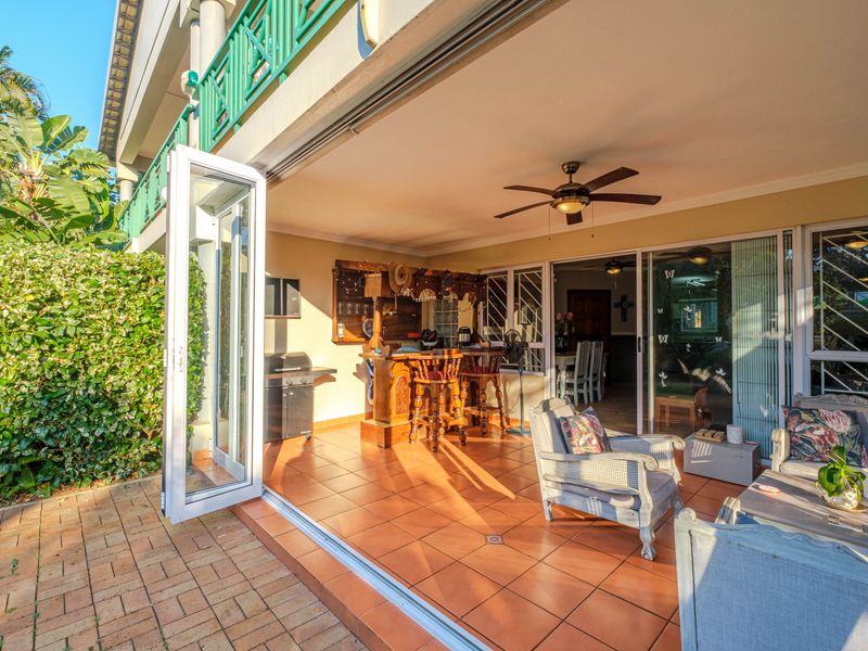 A spacious covered patio featuring tiled flooring, a ceiling fan, and folding glass doors that provide seamless indoor-outdoor flow.