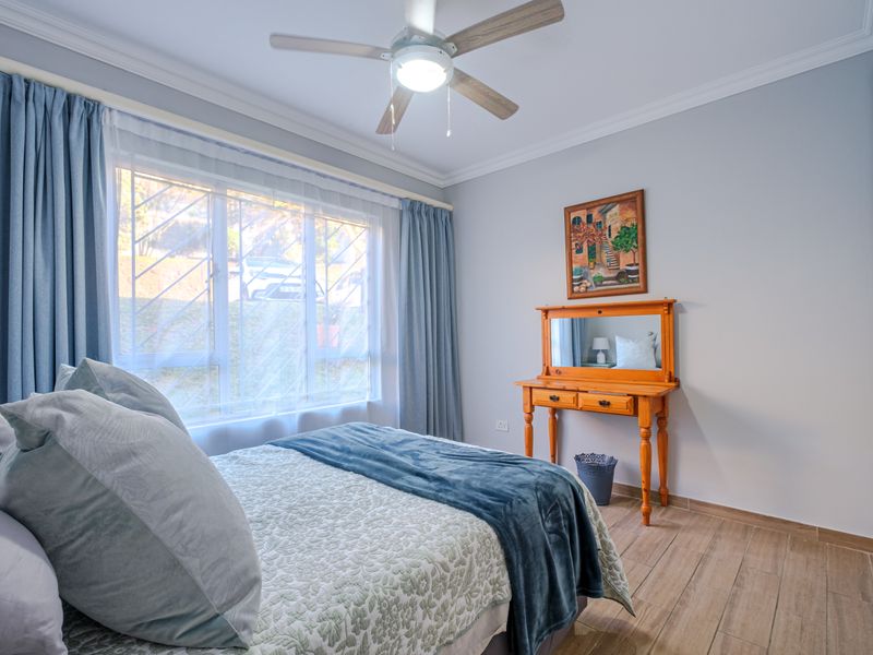 A well-maintained bedroom featuring tiled flooring, a ceiling fan, and built-in cupboards, with natural light provided by a window fitted with security bars.
