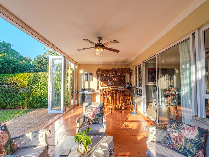 Spacious covered patio featuring tiled flooring, a ceiling fan, and a built-in bar, with seamless access to the garden through bi-fold and sliding glass doors.