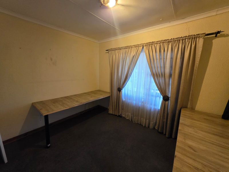A bedroom featuring a built-in desk, carpeted flooring, and window treatments. The space requires cosmetic updates to improve its overall condition.