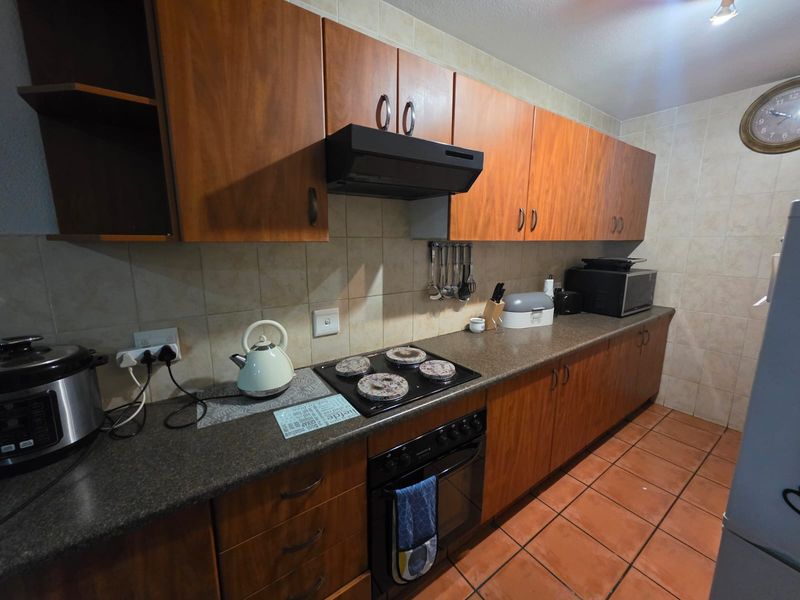 A functional kitchen featuring wood-look cabinetry, dark countertops, an integrated electric hob and oven, and neutral ceramic wall and floor tiles.