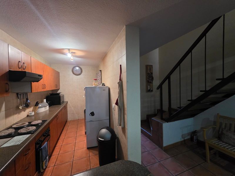 A functional kitchen featuring wooden cabinetry, built-in oven and hob, and tiled flooring, adjacent to an internal staircase.