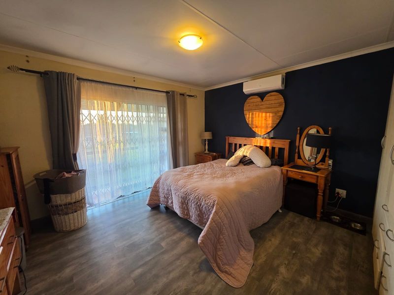 A bedroom featuring laminate flooring, a split-system air conditioner, and a sliding glass door with a security gate leading to the exterior.