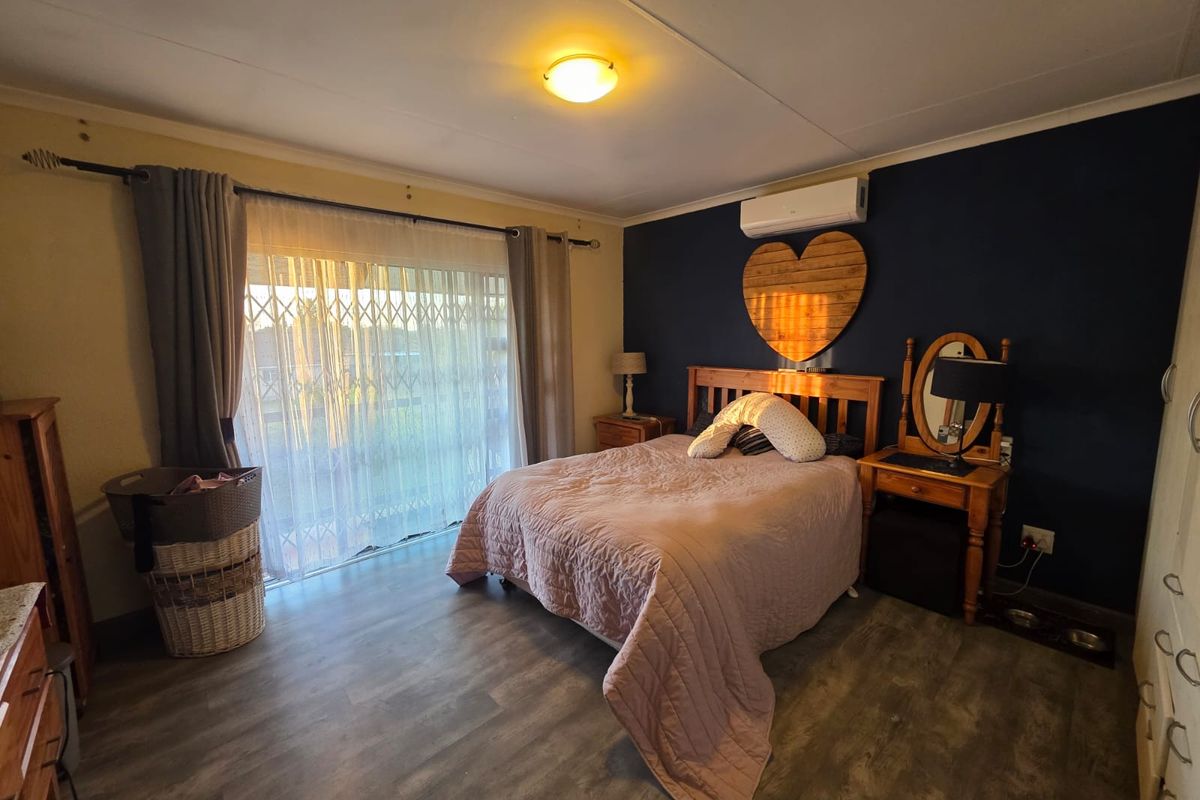 A bedroom featuring laminate flooring, a split-system air conditioner, and a sliding glass door with a security gate leading to the exterior.