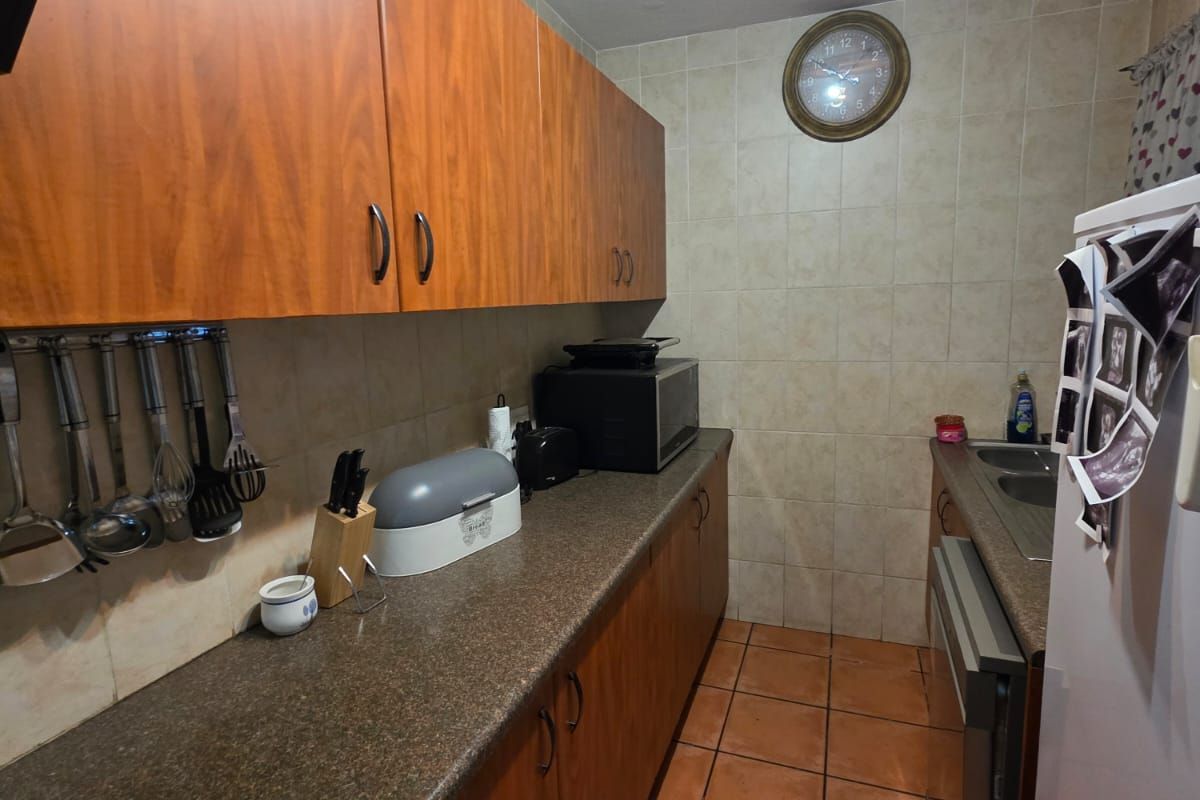 A functional galley-style kitchen featuring wood-look cabinetry, durable laminate countertops, and ceramic tile flooring with full-height wall tiling.