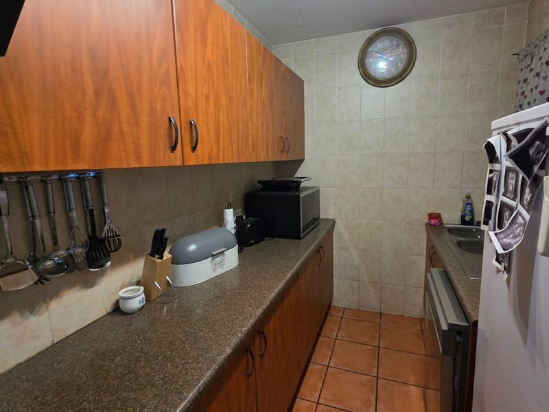 A functional galley-style kitchen featuring wood-look cabinetry, durable laminate countertops, and ceramic tile flooring with full-height wall tiling.