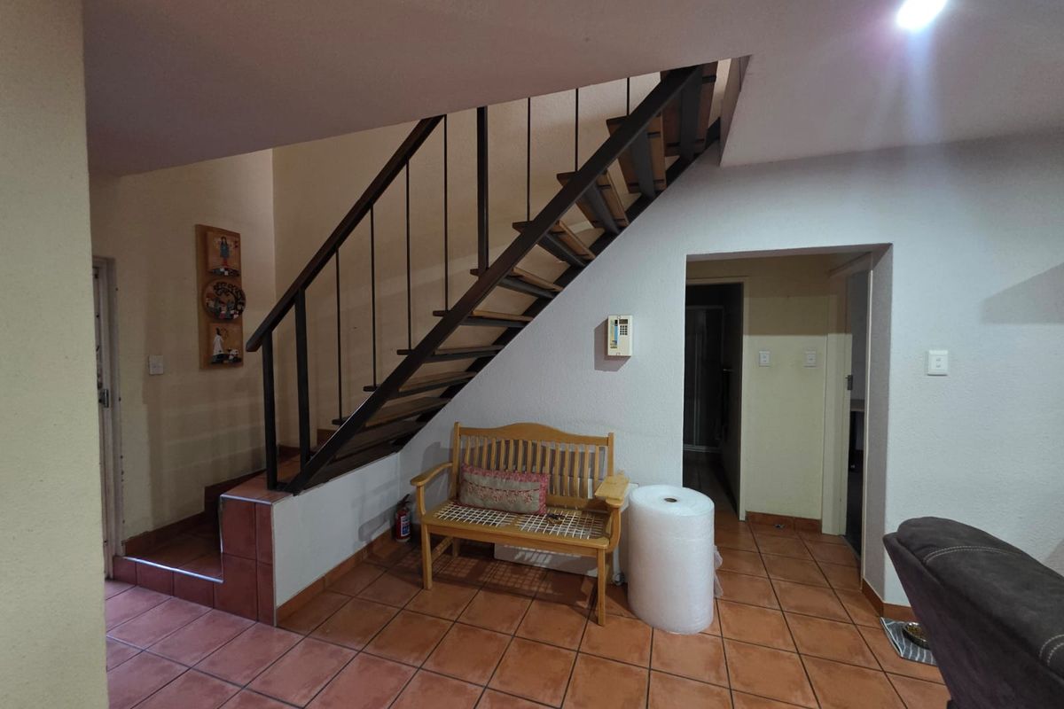 Living area featuring a staircase with a metal balustrade and terracotta floor tiles, providing access to the upper level of the townhouse.