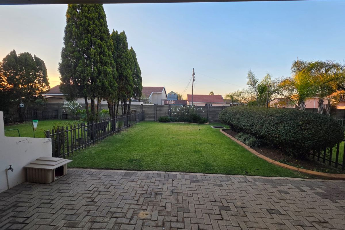 A well-maintained rear garden featuring a paved patio area, manicured lawn, established hedge, and secure perimeter fencing.
