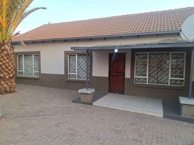 Front elevation of a townhouse featuring a tiled roof, paved driveway, and secure entrance with security gates and aluminium window frames.