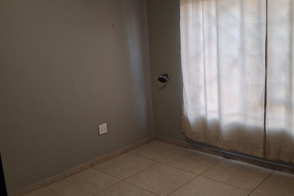 An empty bedroom featuring neutral tiled flooring, grey painted walls, and a fitted curtain rail, providing a blank canvas for personalization.