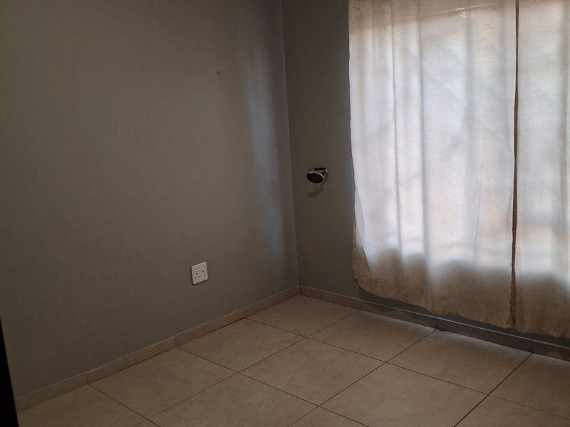 An empty bedroom featuring neutral tiled flooring, grey painted walls, and a fitted curtain rail, providing a blank canvas for personalization.