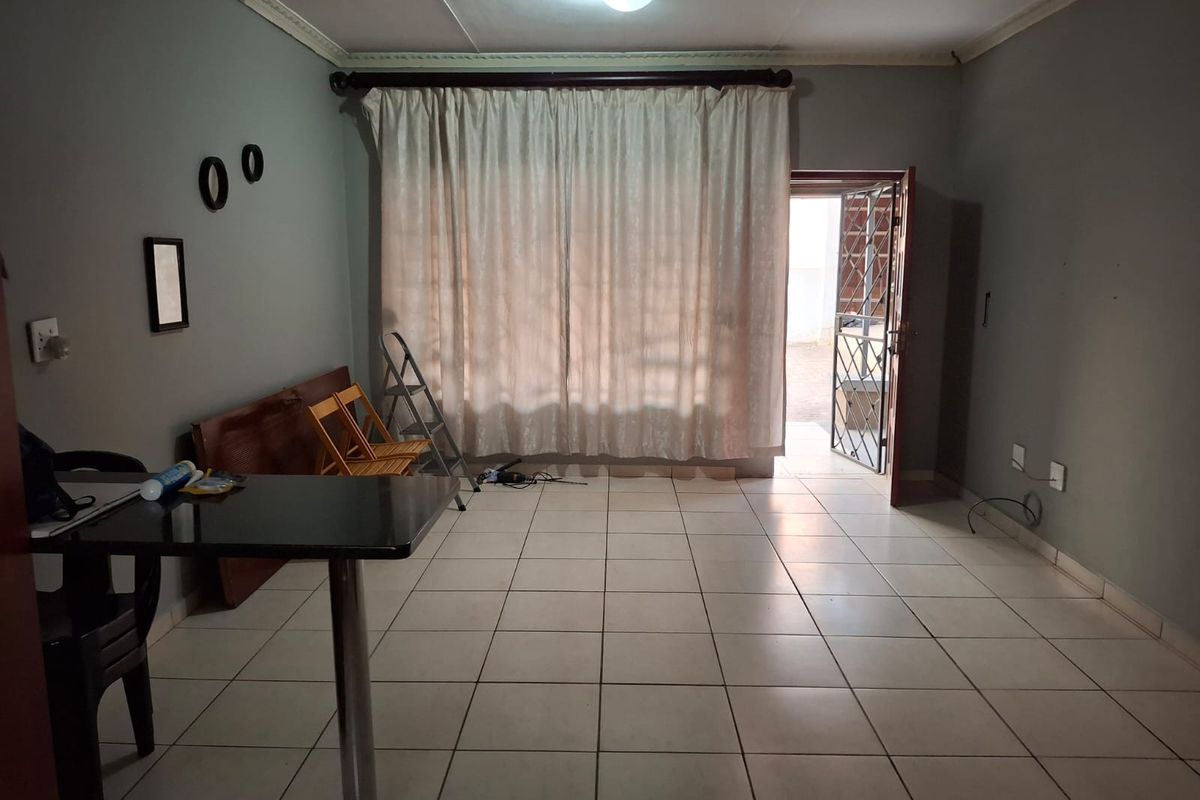 A living area featuring tiled flooring, ceiling cornice detailing, and direct access to the exterior through a security gate.
