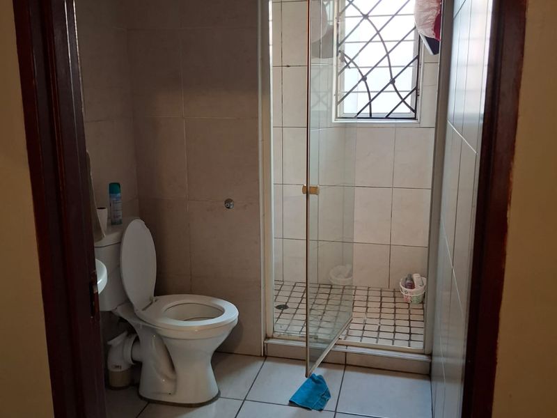 A functional bathroom featuring a toilet and a separate shower enclosure with tiled walls and flooring, requiring some cosmetic updates.