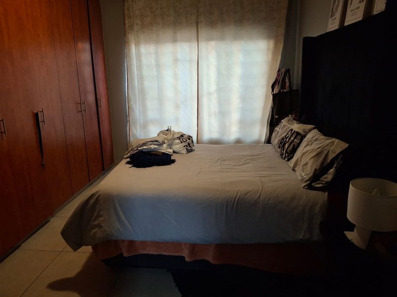 A bedroom featuring built-in wooden cupboards and tiled flooring, offering a functional space with natural light.