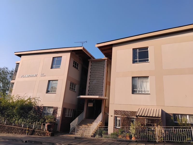 Front elevation of Flamboyant Court apartment building featuring a central staircase entrance, decorative breeze block detailing, and a combination of brick and rendered facade.