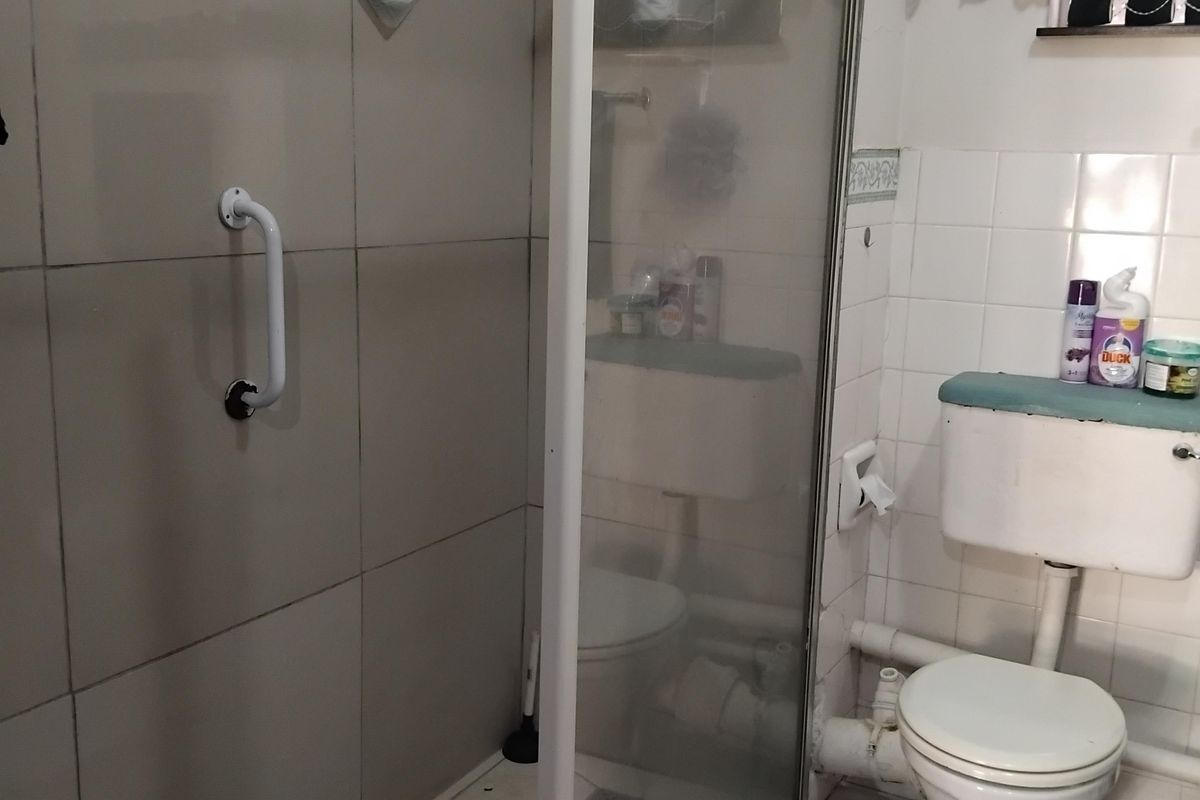 A functional bathroom featuring a shower enclosure with a grab rail, a standard toilet, and tiled finishes throughout.