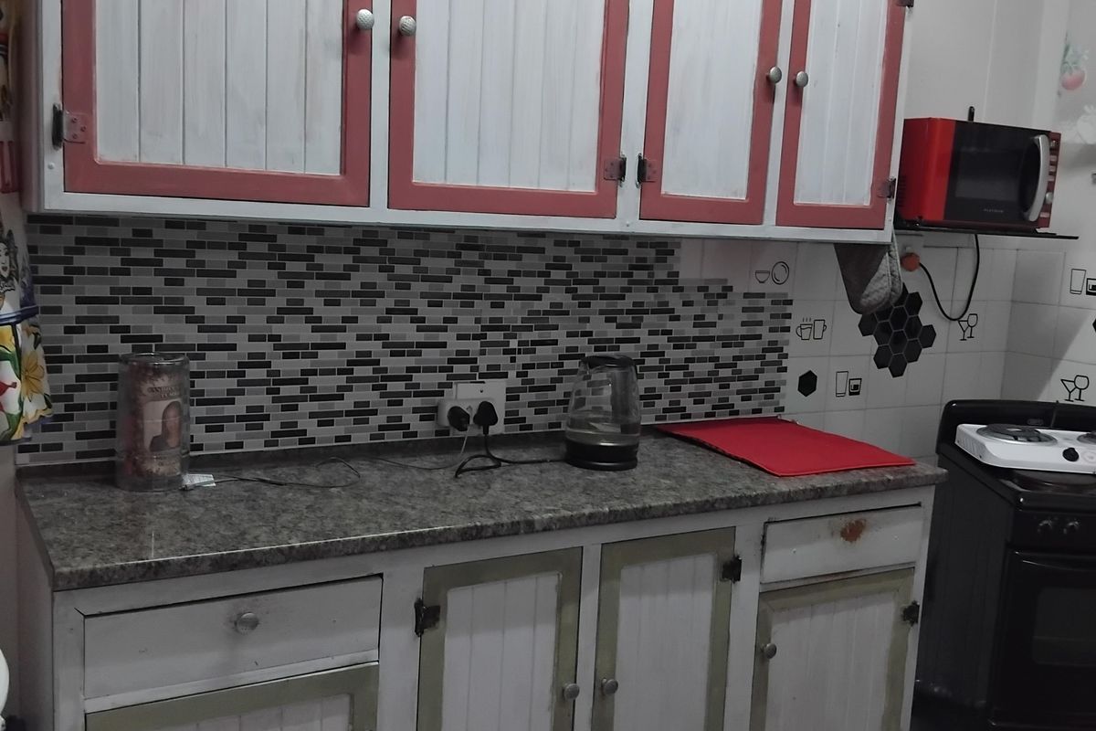 A kitchen area featuring granite countertops, mosaic tile backsplash, and custom painted cabinetry with visible signs of wear.