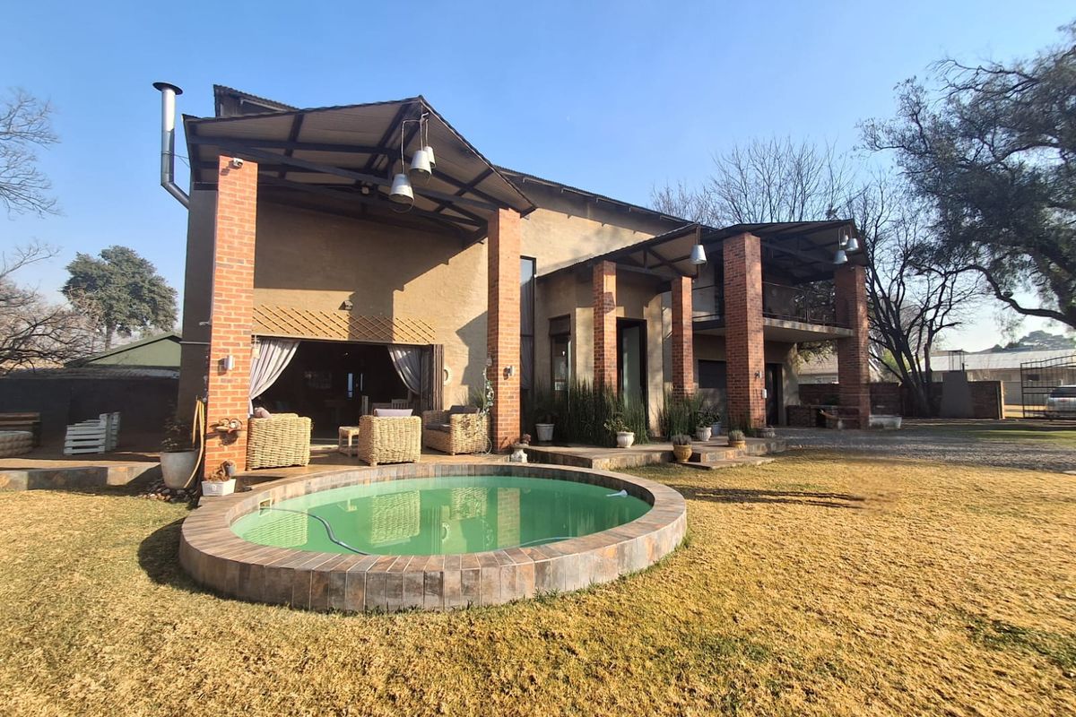 Rear view of the property featuring a circular swimming pool, covered patio area with brick pillars, and a balcony overlooking the garden.
