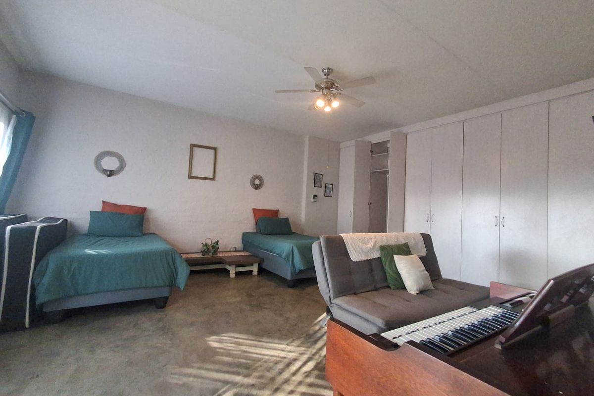 Spacious bedroom featuring built-in cupboards, a ceiling fan, and concrete flooring, offering a functional layout with ample storage space.