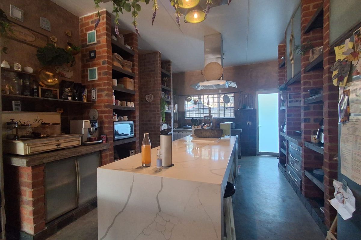 A rustic-style kitchen featuring exposed brick pillars, a large stone-topped island, concrete flooring, and integrated shelving with a modern stainless steel extractor fan.