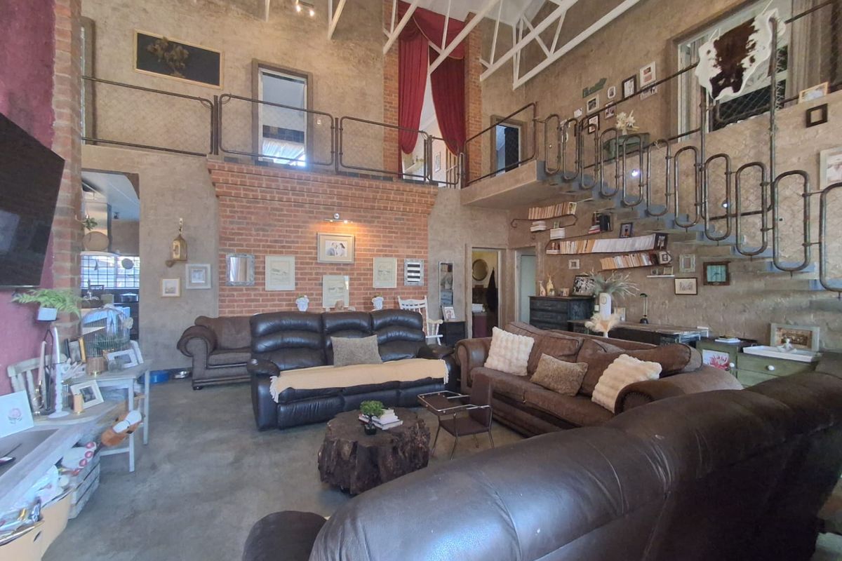 Spacious double-volume living room featuring exposed brickwork, industrial-style metal mezzanine balustrades, exposed roof trusses, and polished concrete flooring.