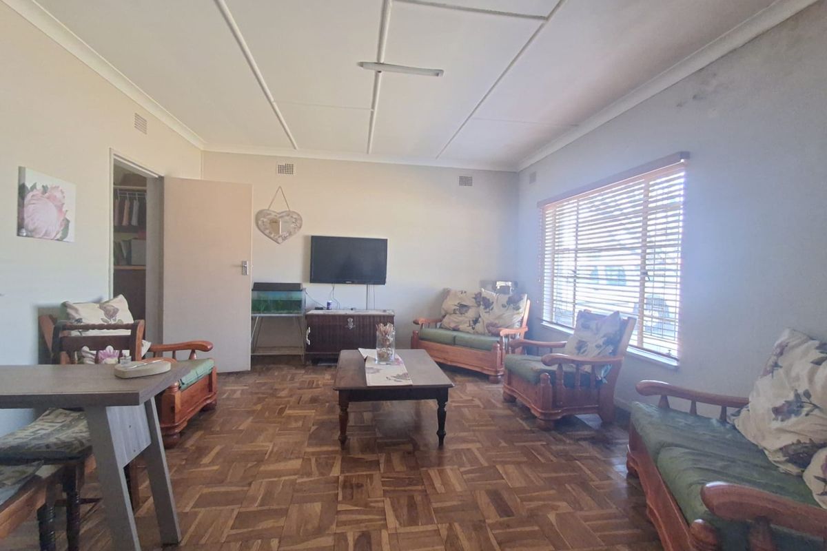 A living room featuring traditional parquet flooring, venetian blinds, and a tiled ceiling, offering a dated interior space ready for modernization.