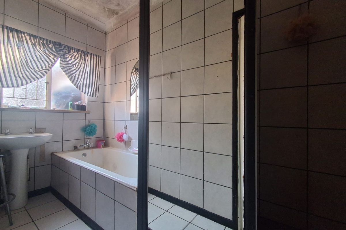 A dated bathroom featuring a pedestal basin and built-in bathtub, requiring ceiling repairs and cosmetic updates to improve the overall condition.