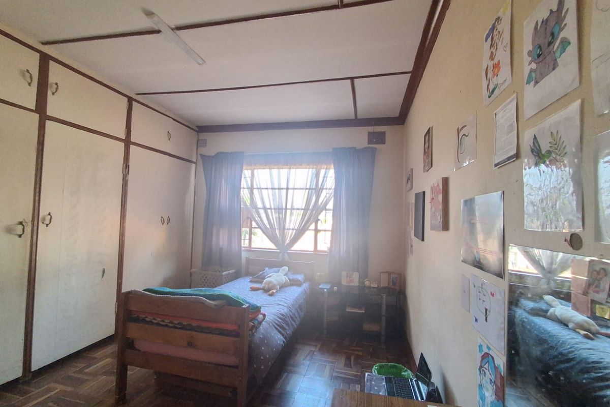 A bedroom featuring parquet flooring, built-in cupboards, and an exposed beam ceiling, offering a functional space with potential for cosmetic updates.