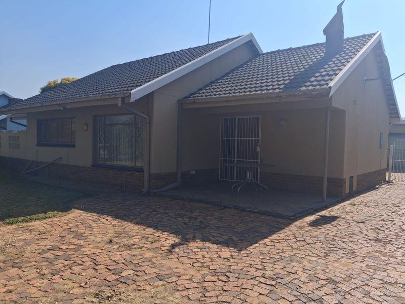 Rear view of the house featuring a covered patio, brick paved driveway, and tiled roof structure.
