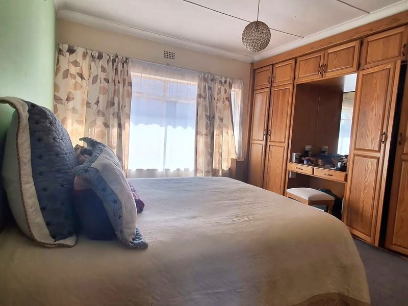 A bedroom featuring built-in wooden wardrobes with an integrated vanity and a wall-mounted air conditioning unit.