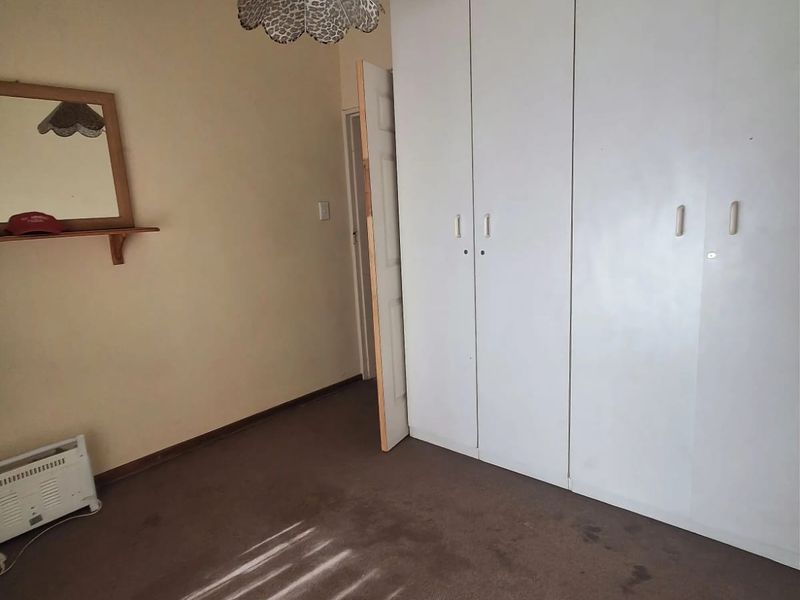 A bedroom featuring built-in cupboards, coving, and carpeted flooring. The room is vacant and requires cosmetic updates to improve its overall condition.