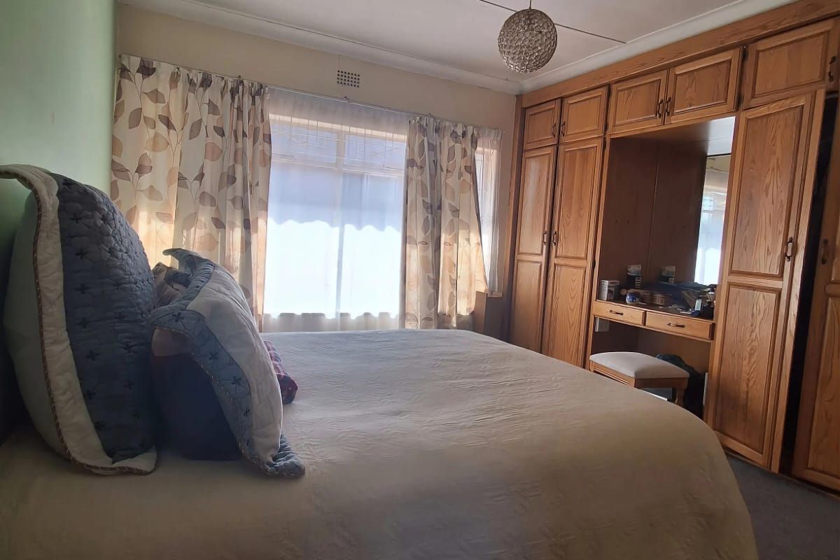 A bedroom featuring a large built-in wooden wardrobe with an integrated vanity unit and a wall-mounted air conditioning unit.