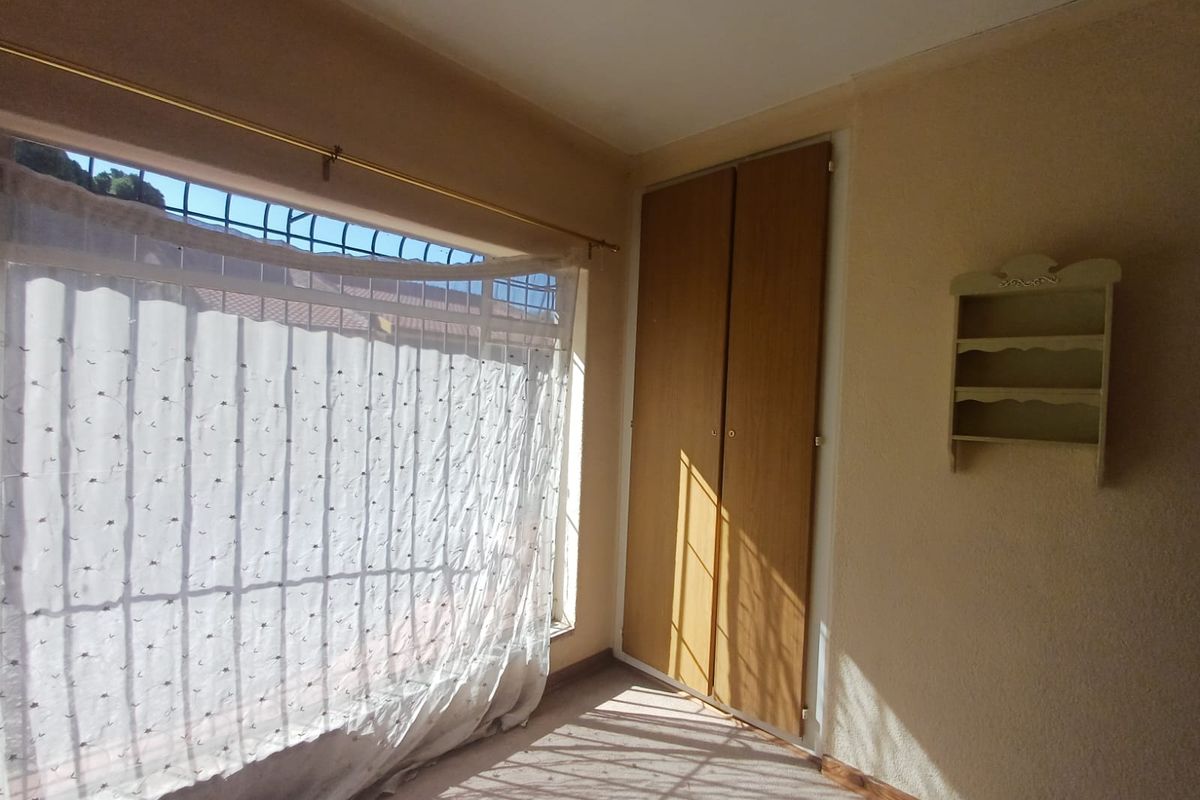 A vacant bedroom featuring a built-in wardrobe, carpeted flooring, and large windows fitted with security bars.