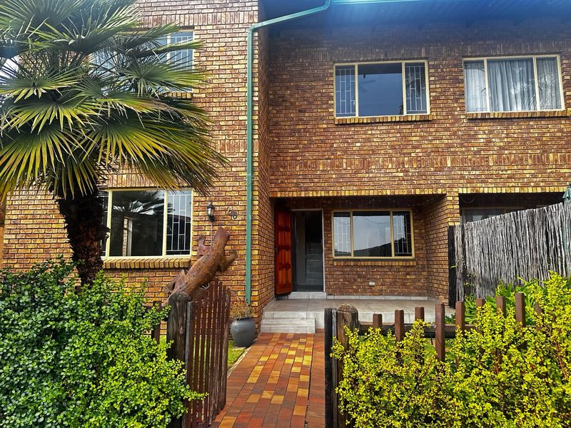 Front elevation of a face brick townhouse featuring a paved walkway, timber fencing, and security-fitted windows.