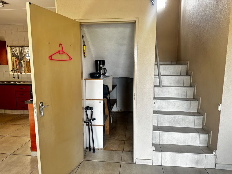 A utility storage space located under a tiled staircase, adjacent to the kitchen area in this townhouse.