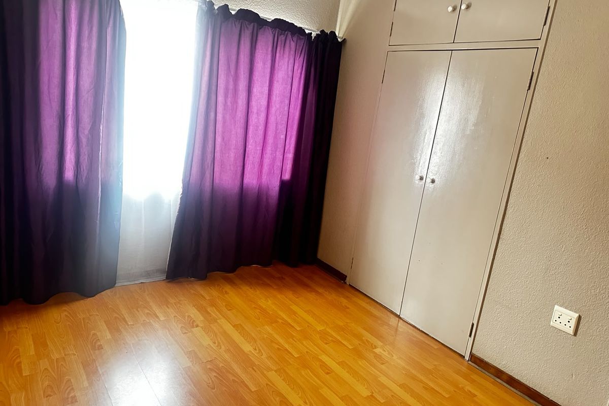 A bright, empty bedroom featuring laminate flooring and built-in cupboards with overhead storage.