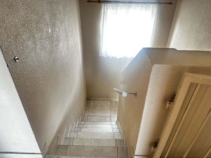 A tiled staircase featuring a handrail and safety gate, leading to a landing area with a window.
