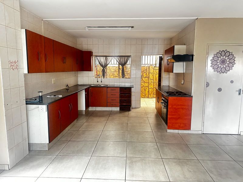 A functional kitchen featuring wood-tone cabinetry, dark countertops, built-in oven and hob, and neutral ceramic floor tiling throughout.