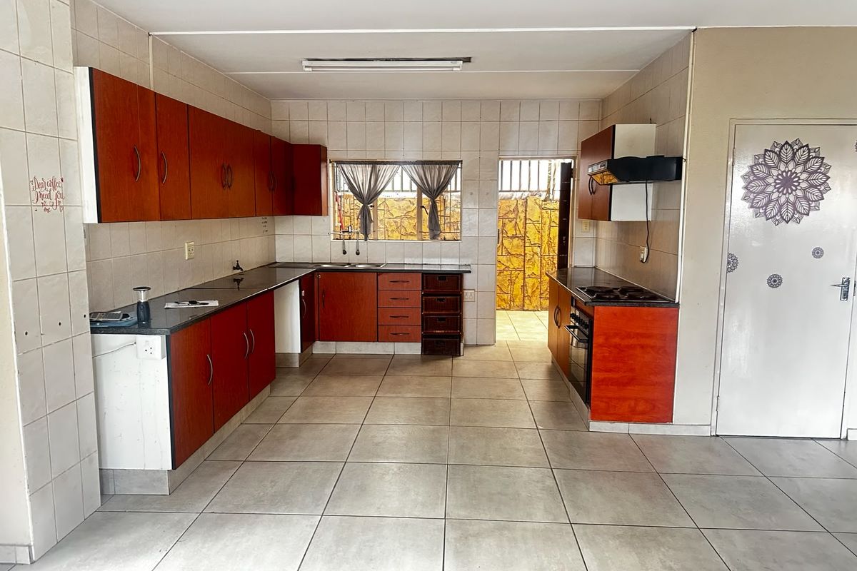 A functional kitchen featuring wood-tone cabinetry, dark countertops, built-in oven and hob, and neutral ceramic floor tiling throughout.