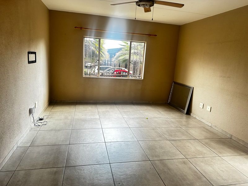 An empty living room featuring tiled flooring, a ceiling fan, and a window with security bars, offering a blank canvas for potential interior updates.