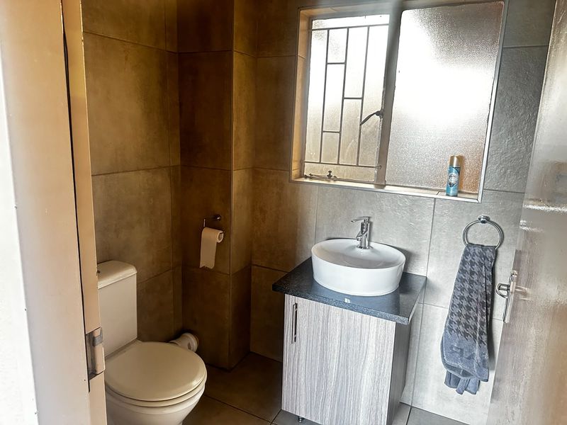 A compact bathroom featuring a modern vessel sink on a vanity cabinet, a toilet, and neutral wall tiling with a window for natural light.