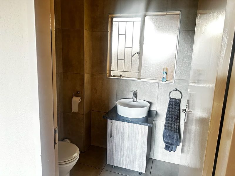 A compact bathroom featuring a modern vessel sink on a vanity cabinet, tiled walls, and a toilet, with natural light from a window.