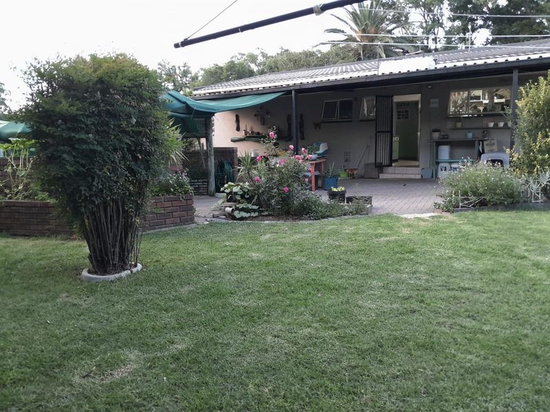 A rear view of the property featuring a lawn, brick-paved patio area, and a covered veranda with established garden beds.