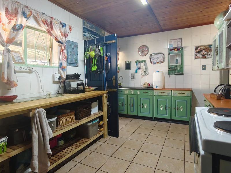 A functional kitchen featuring tiled flooring, timber ceiling, and traditional cabinetry with a tiled splashback and integrated sink area.
