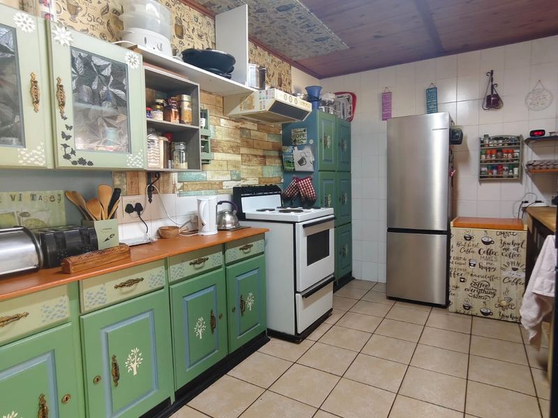 A dated kitchen featuring green cabinetry, tiled flooring, and a timber ceiling, offering significant potential for modernization and renovation.