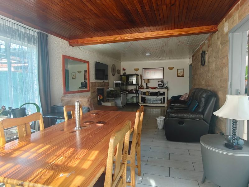 Open plan living and dining area featuring a warm timber ceiling, stone accent wall, and neutral ceramic floor tiles with access to the outdoors.