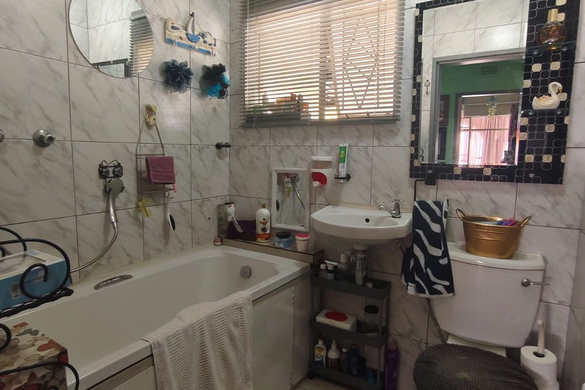 A functional bathroom featuring a bathtub, pedestal basin, and toilet with full-height wall tiling and neutral floor tiles.