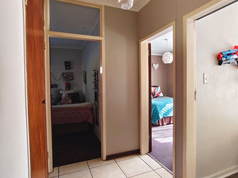 A tiled hallway providing access to multiple bedrooms, featuring neutral wall tones, a built-in cupboard, and a security camera.