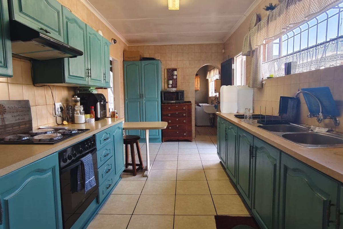 A functional galley-style kitchen featuring teal cabinetry, tiled flooring, built-in oven with gas hob, and a double basin sink.