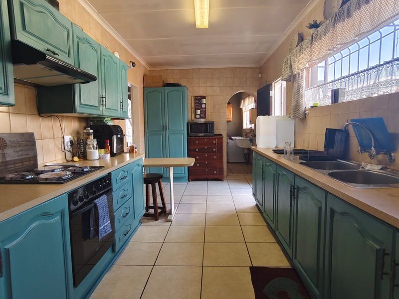 A functional galley-style kitchen featuring teal cabinetry, tiled flooring, built-in oven with gas hob, and a double basin sink.